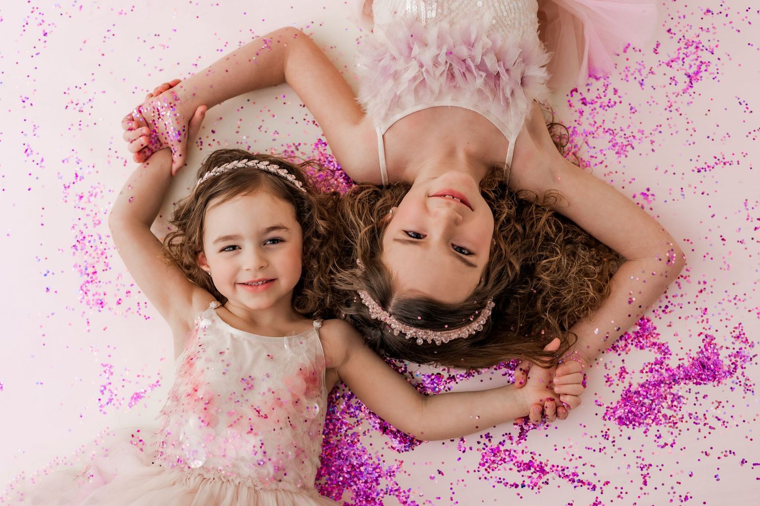 two little girls with princess crowns laying in pink glitter