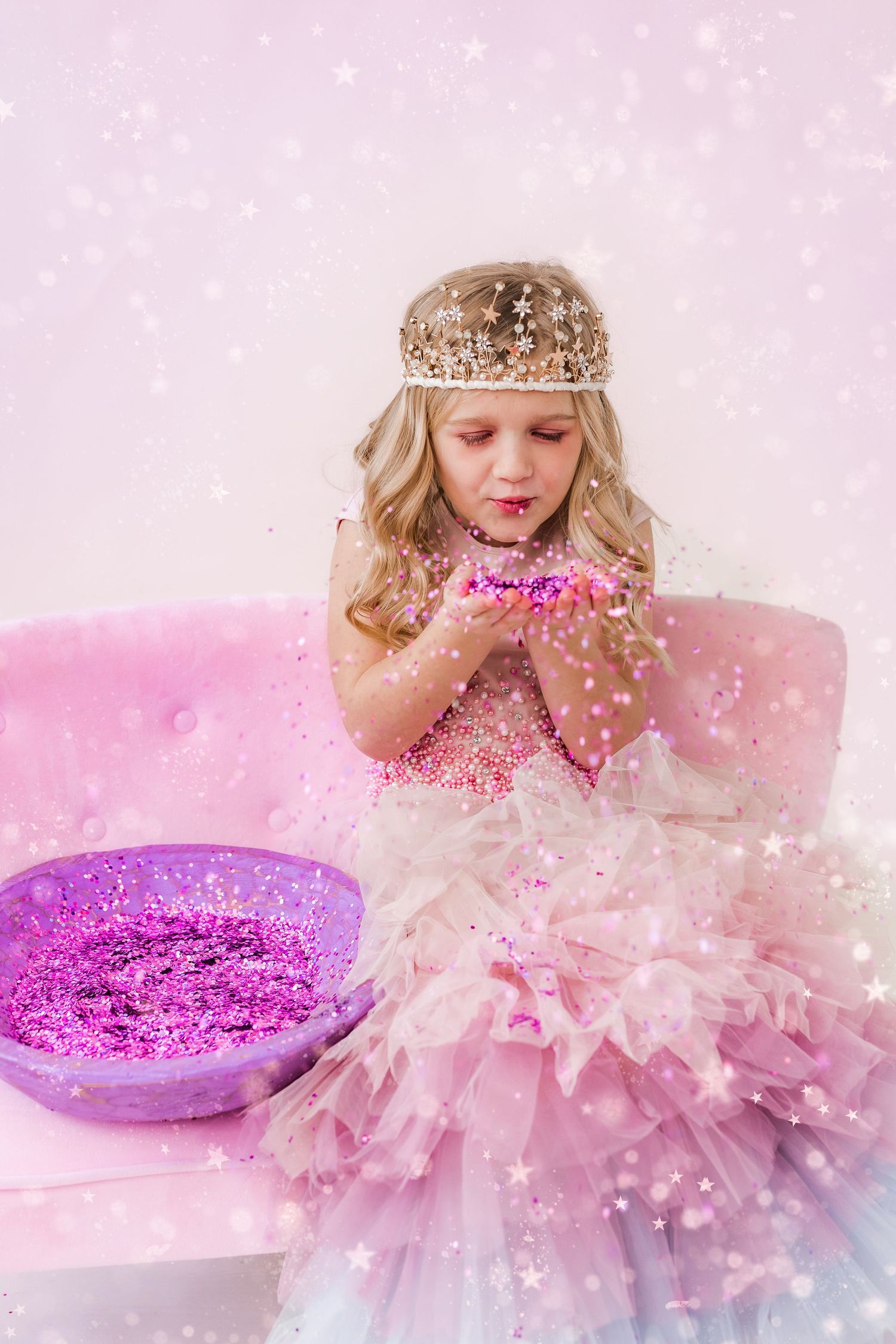 little girl in tiara blowing pink glitter on a pink couch