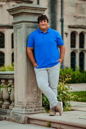 senior portrait boy looks confident, strong and stylish with stone mansion looming in background