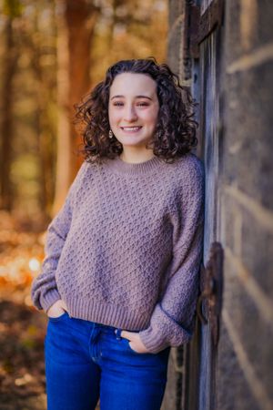 High school senior posing confidently outdoors with a natural smile, dressed in stylish attire, with soft golden sunlight