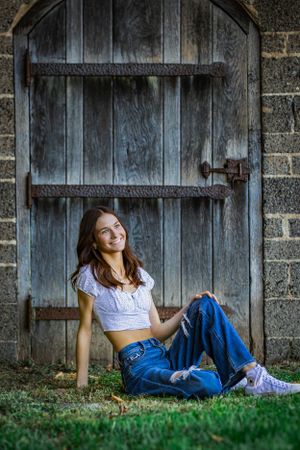 An awesome posed senior portrait of a girl lazily sitting in front of a wooden door