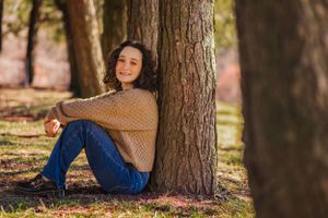 High school senior posing confidently outdoors with a natural smile, dressed in stylish attire, with soft golden sunlight