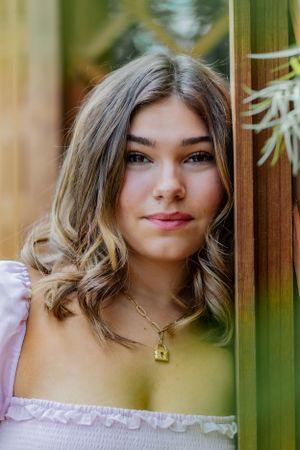 Upclose and personal this headshot features a girl leaning against a red wood trellis with vibrant green vines