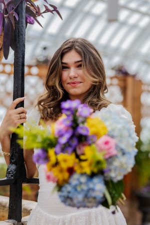 A girl holds a bouquet of flowers towards the camera, her framed face smiles