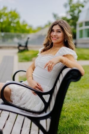 A classic senior portrait, sitting on a wooden bench in a poised pose