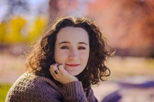 High school senior posing confidently outdoors with a natural smile, dressed in stylish attire, with soft golden sunlight