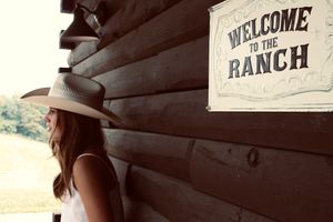 Creative angles features a sign 'welcome to the ranch' in the foreground. The cowgirl is in the background
