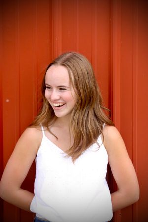 A vibrant red barn door is the backdrop for this stunning senior portrait of a girl laughing and enjoying her youth