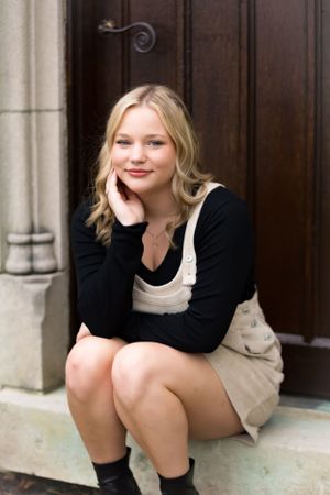 Nothing by attitude in this senior portrait of a girl posed sitting against a wooden door.