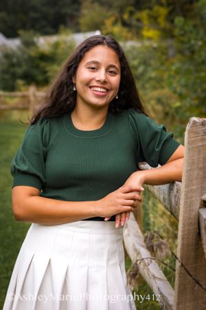 A classic senior portrait, hands resting on a wooden fence in a poised pose