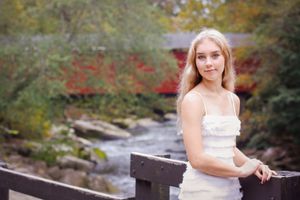 Poised on a wooden fence, the red covered bridge behind the girl is the star of this senior portrait