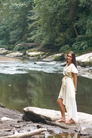Nature and natural beauty in this senior portrait of a girl standing on rocks as a large stream flows behind her