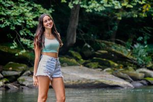Enjoying the great outdoors wading in a shallow stream this senior portrait feature a girl kicking up water and laughing