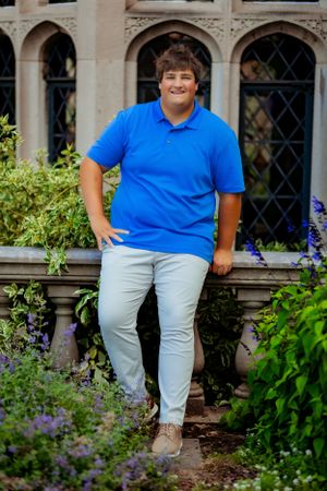 Senior portrait boy leaning on stone ledge confidently and casually