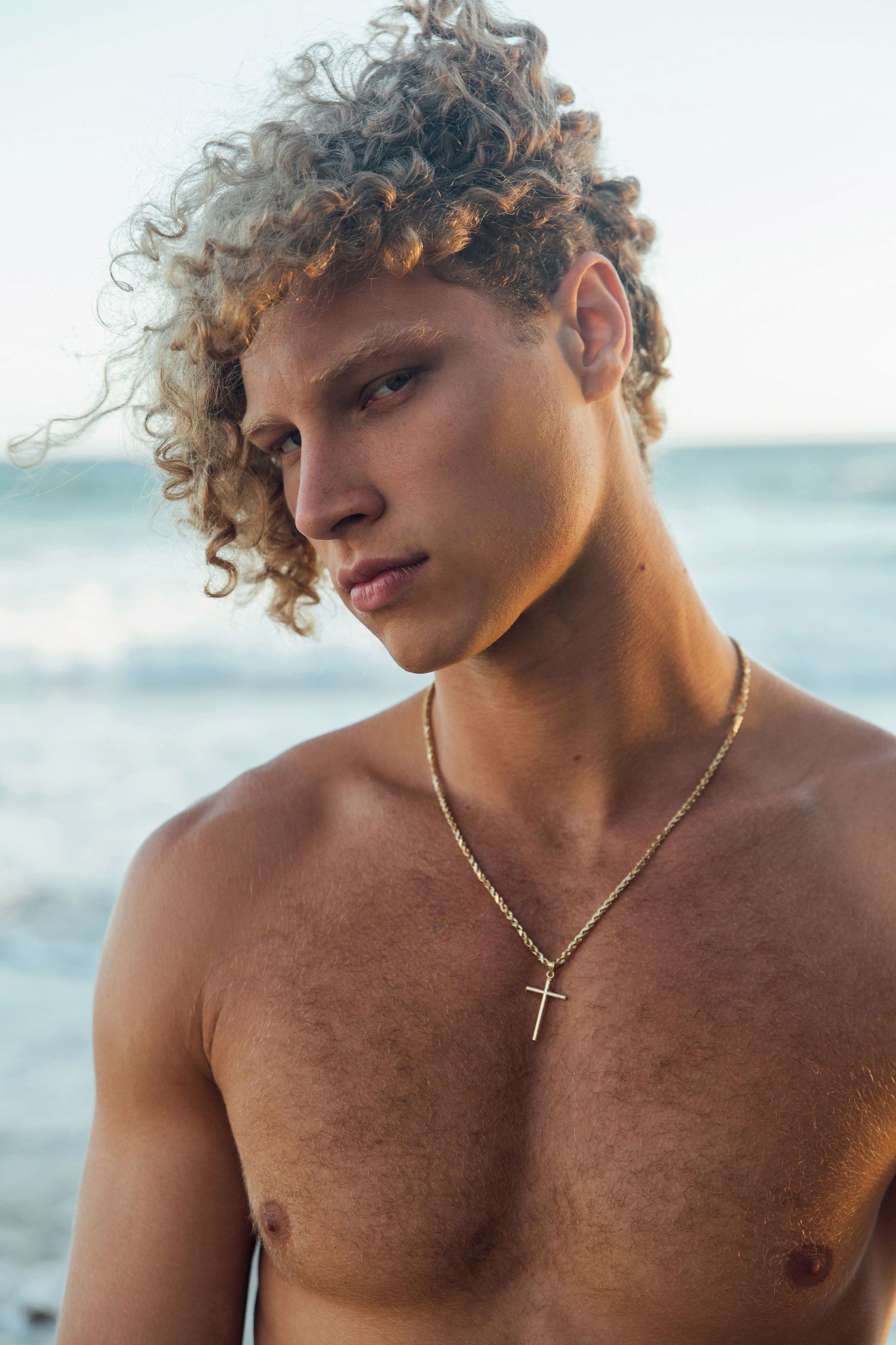 Curly blonde male model standing on beach with wind blowing in hair, San Clemente beach fashion editorial