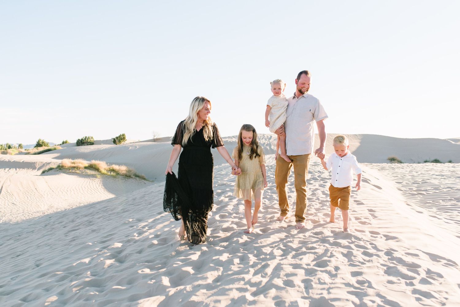 A family of five walks together along pristine white sand dunes at sunset.