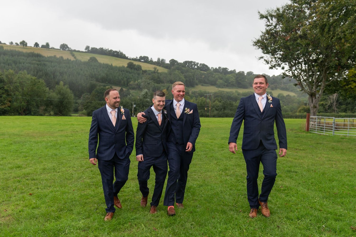 Groomsmen in navy suits walking across a green hillside field.