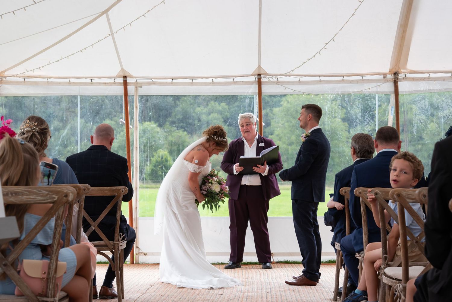 Wedding ceremony under a white tent with guests seated in rows.