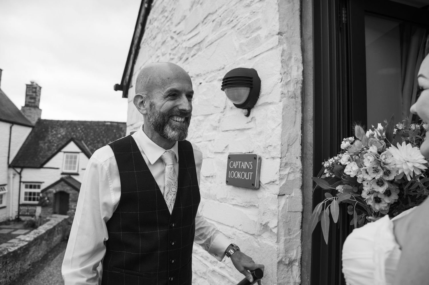 Elegant wedding party men in navy suits walk along a white stone wall at an outdoor venue.