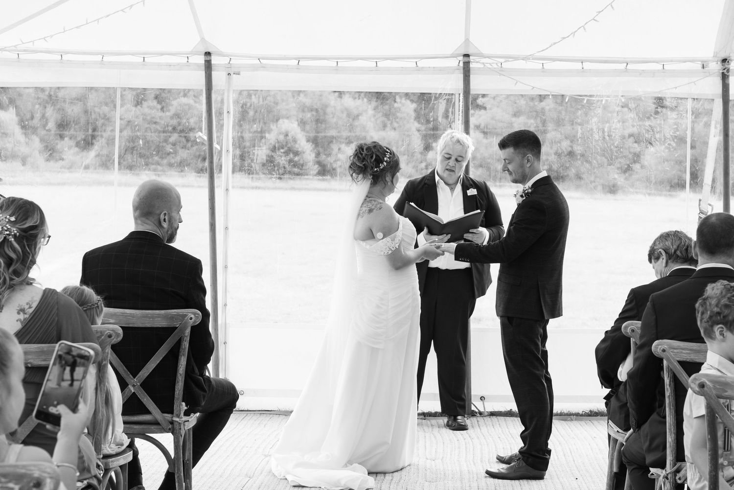 Wedding ceremony in a white marquee tent with guests seated in rows.