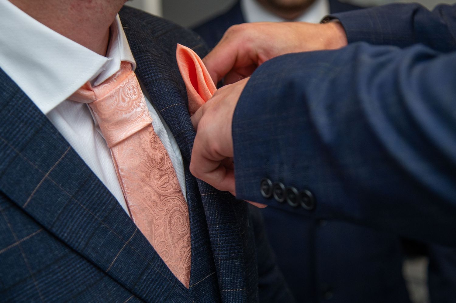 Detail shot of a pink necktie and navy blue suit jacket.