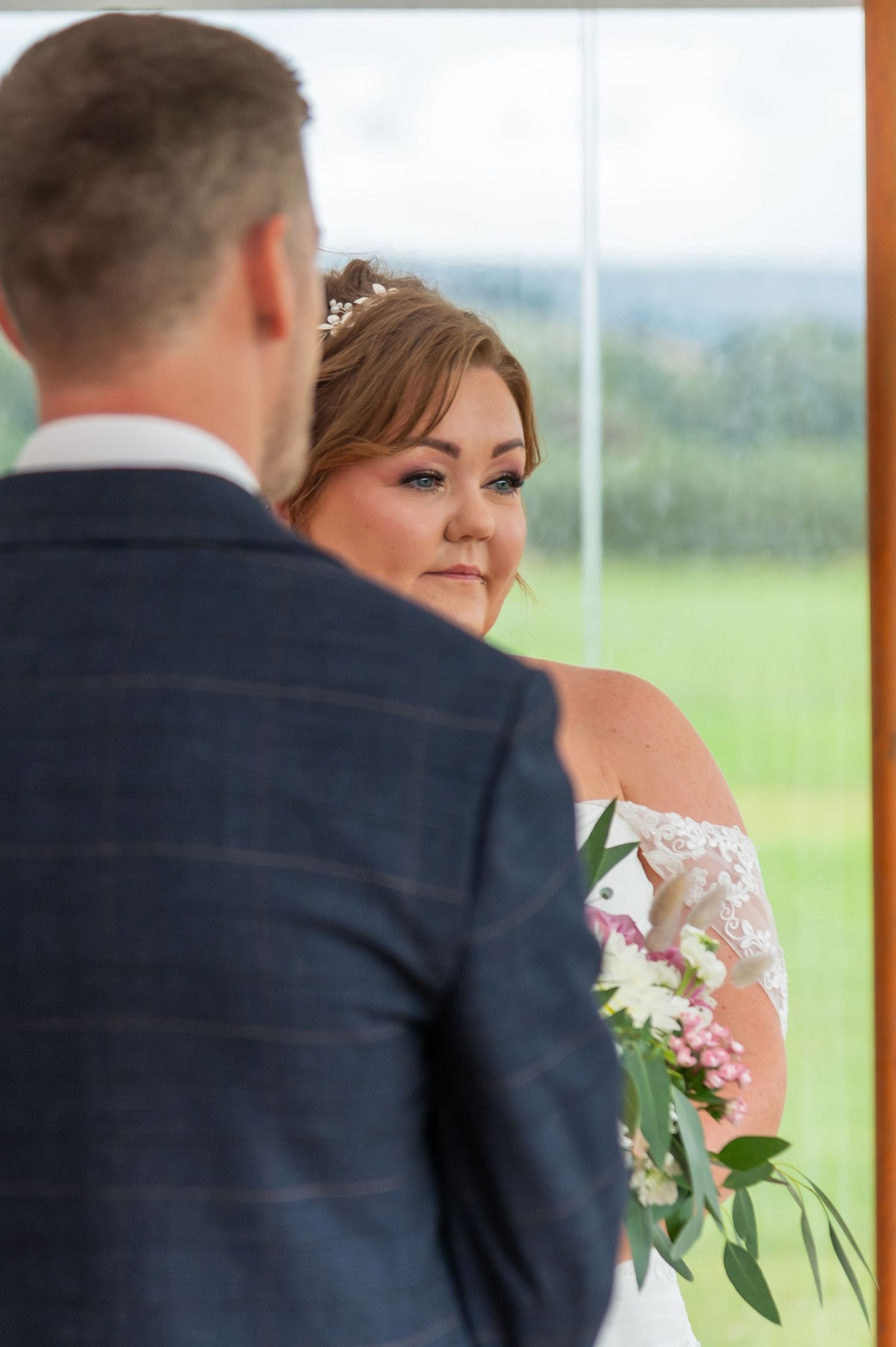 A romantic wedding ceremony moment captured through a window with rolling hills in the background.