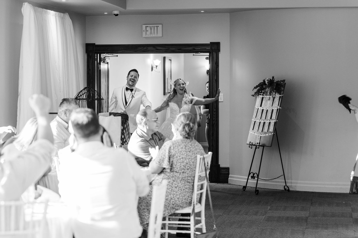 Black and white photo of a wedding party dancing and celebrating in an elegant indoor venue.