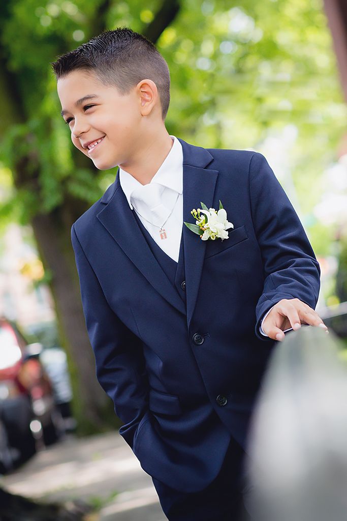Young attendant in a navy suit and boutonniere smiles outdoors.
