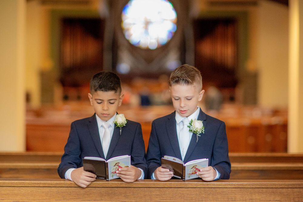 Two young boys in formal attire reading prayer books together in a church pew.