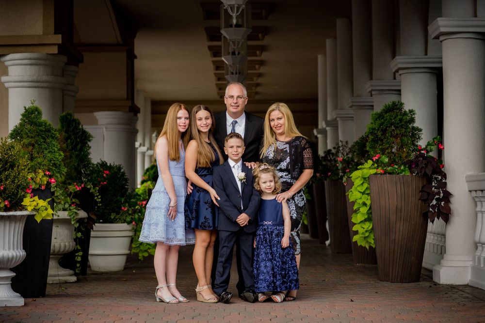 Family portrait of five people dressed in formal attire standing under ornate archway with floral decorations.