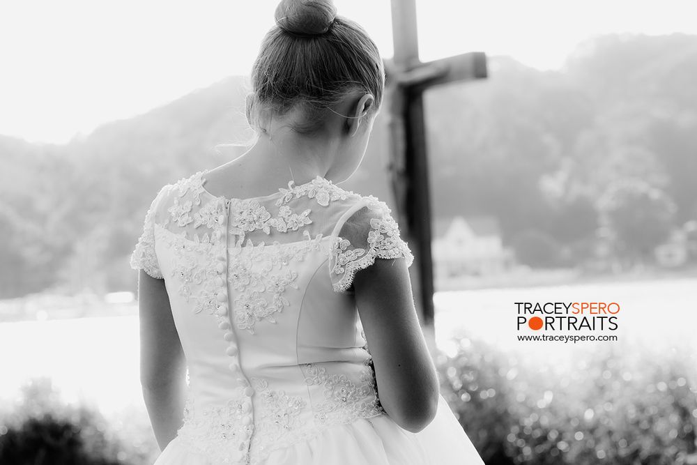 Back view of person in white lace dress standing near cross outdoors in black and white photo.