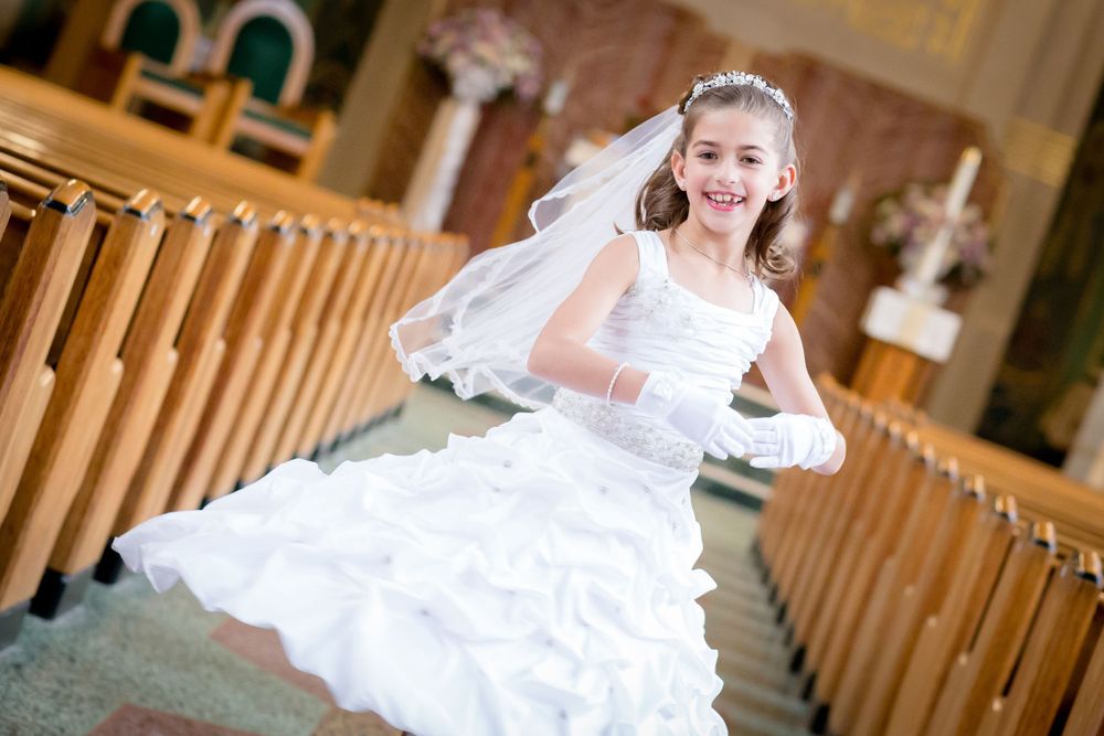 Young girl in white communion dress twirling at church.