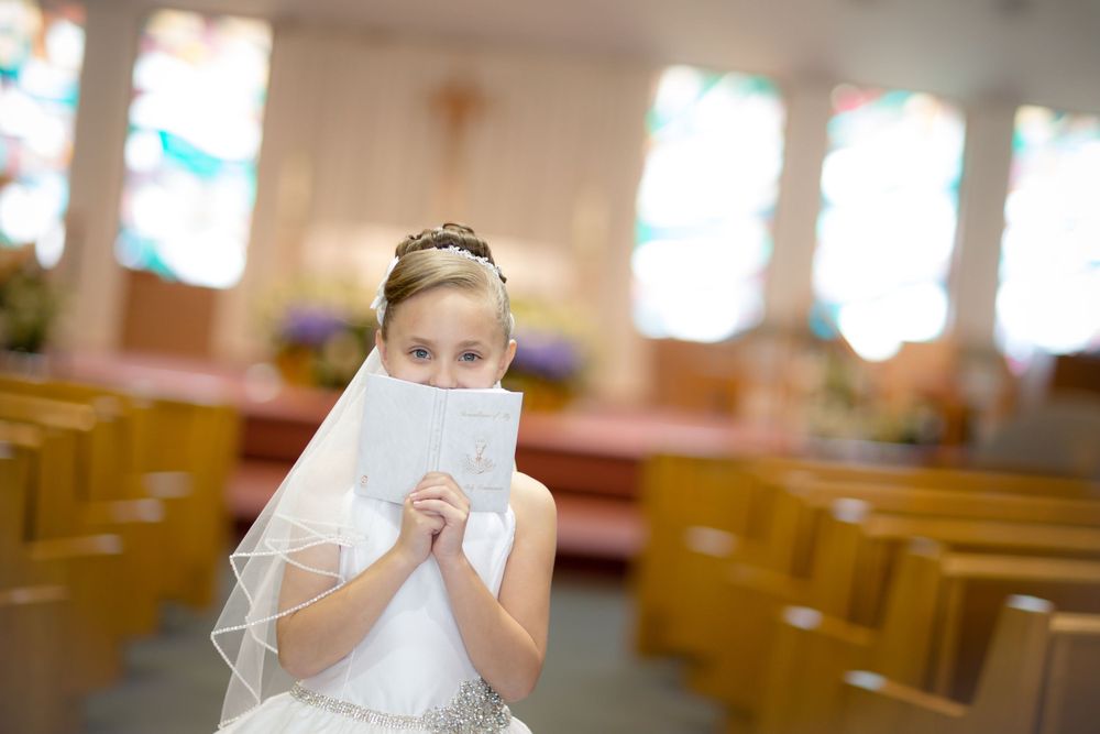 A child in white holding a prayer book in a church sanctuary during a special celebration.