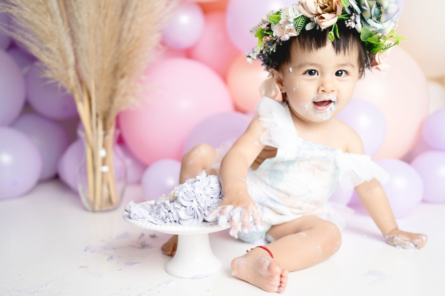 Charming first birthday photoshoot with floral crown and pink balloon backdrop.