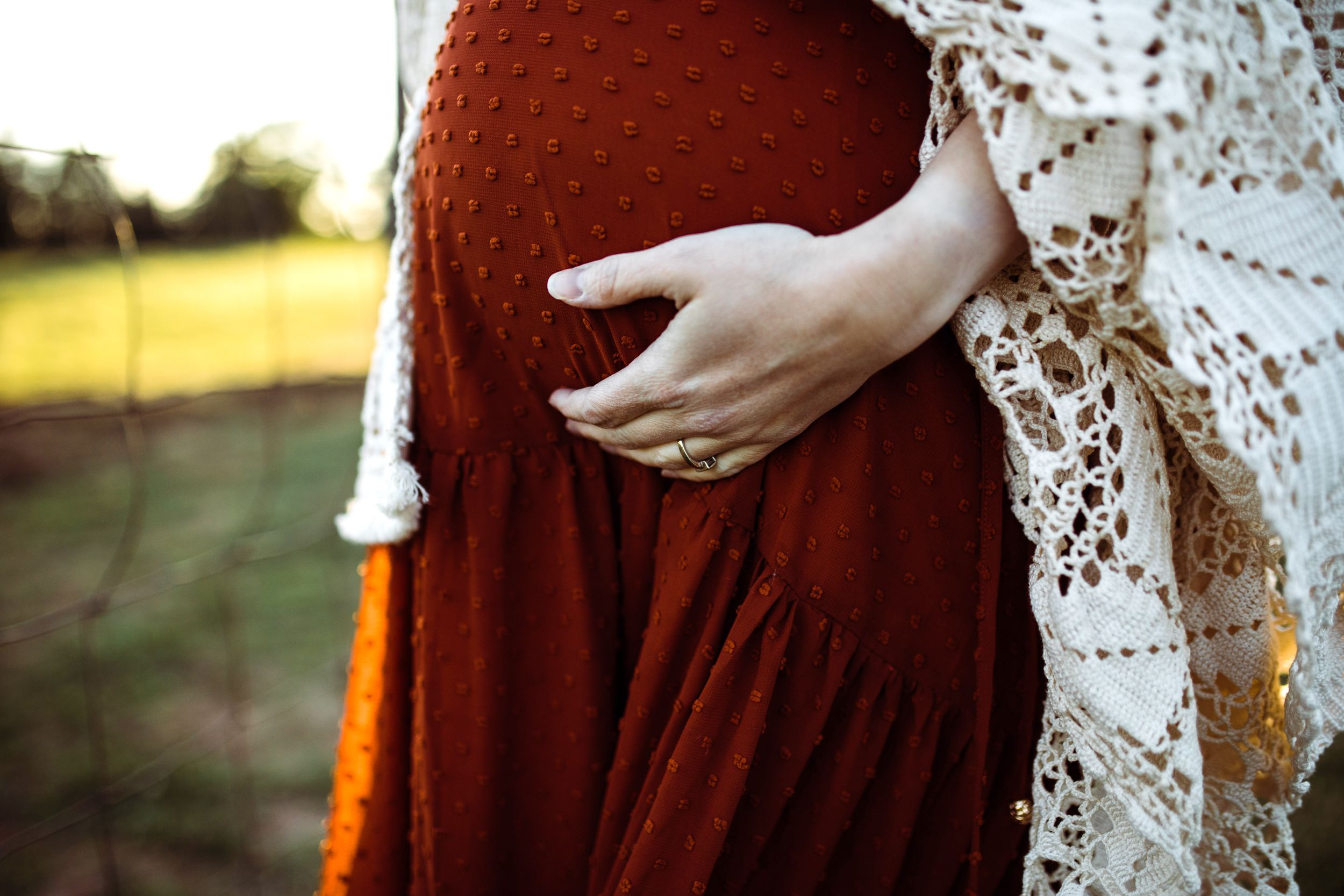 Close-up of pregnant woman in rust dress holding baby bump with lace wrap.