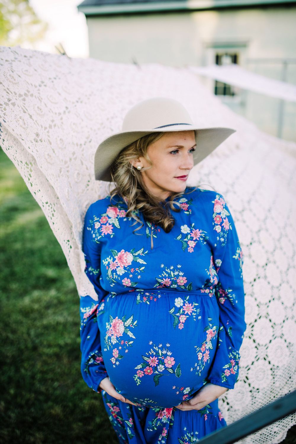 Pregnant woman in blue floral dress and wide-brim hat holding baby bump.