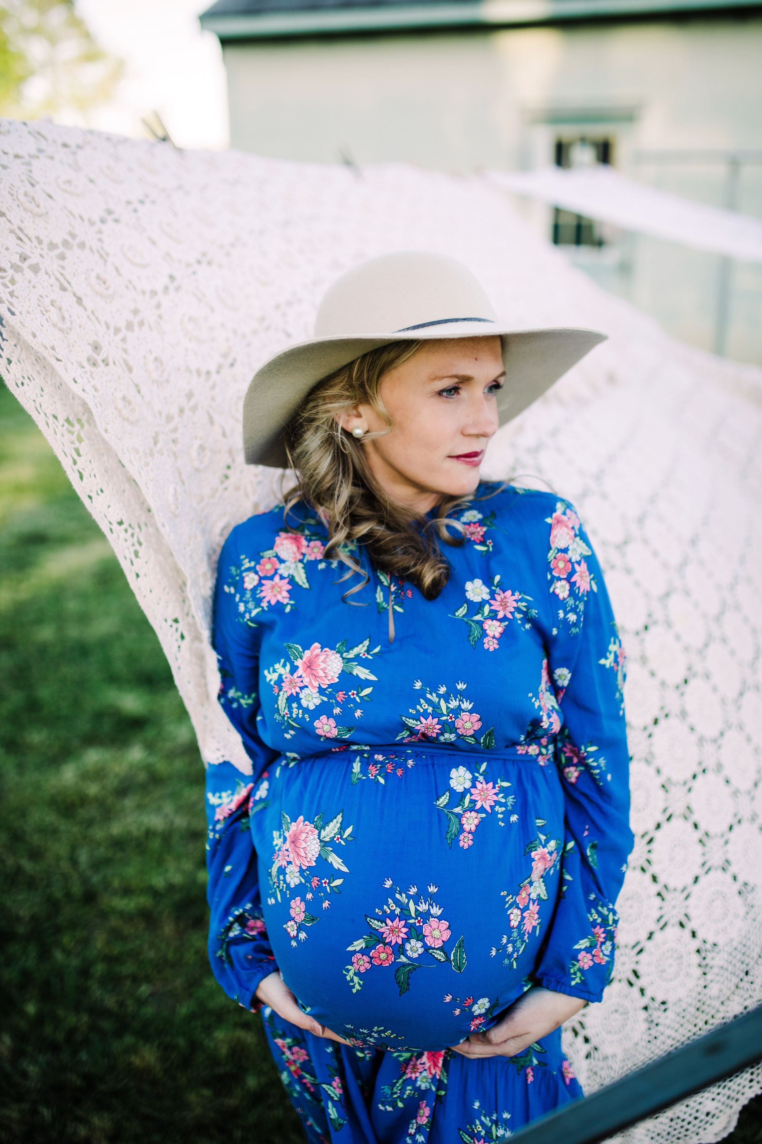 Pregnant woman in blue floral dress and wide-brim hat holding baby bump.