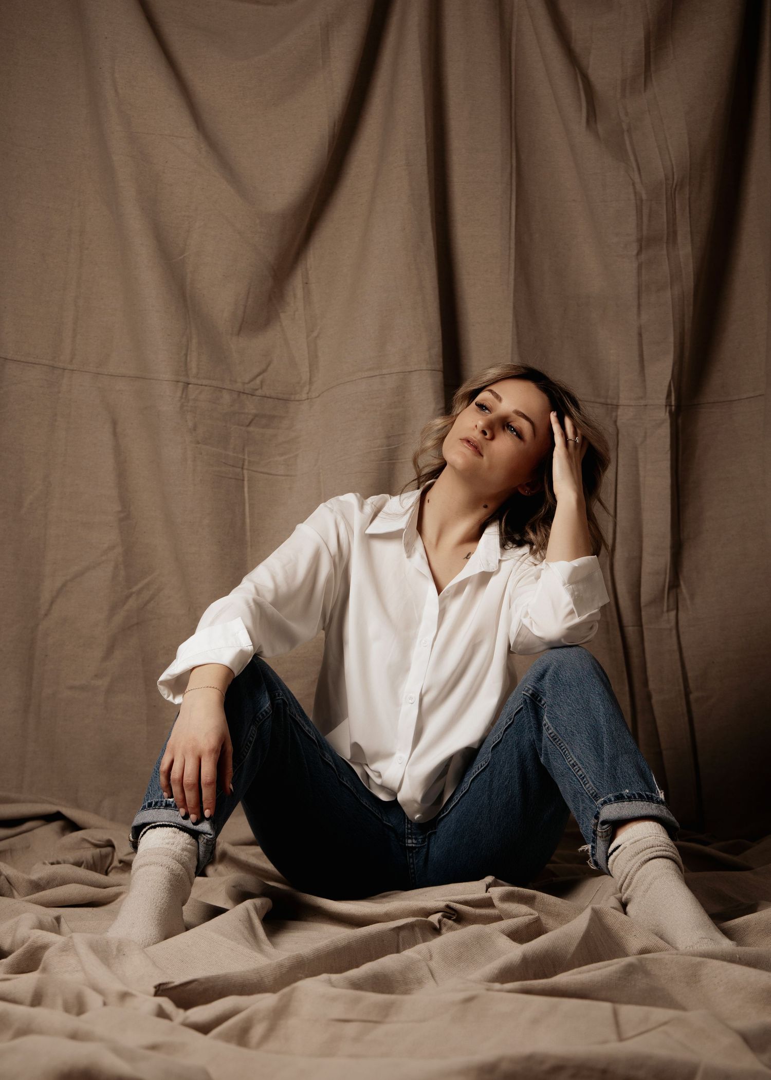 Casual portrait with white button down shirt and jeans against brown backdrop.
