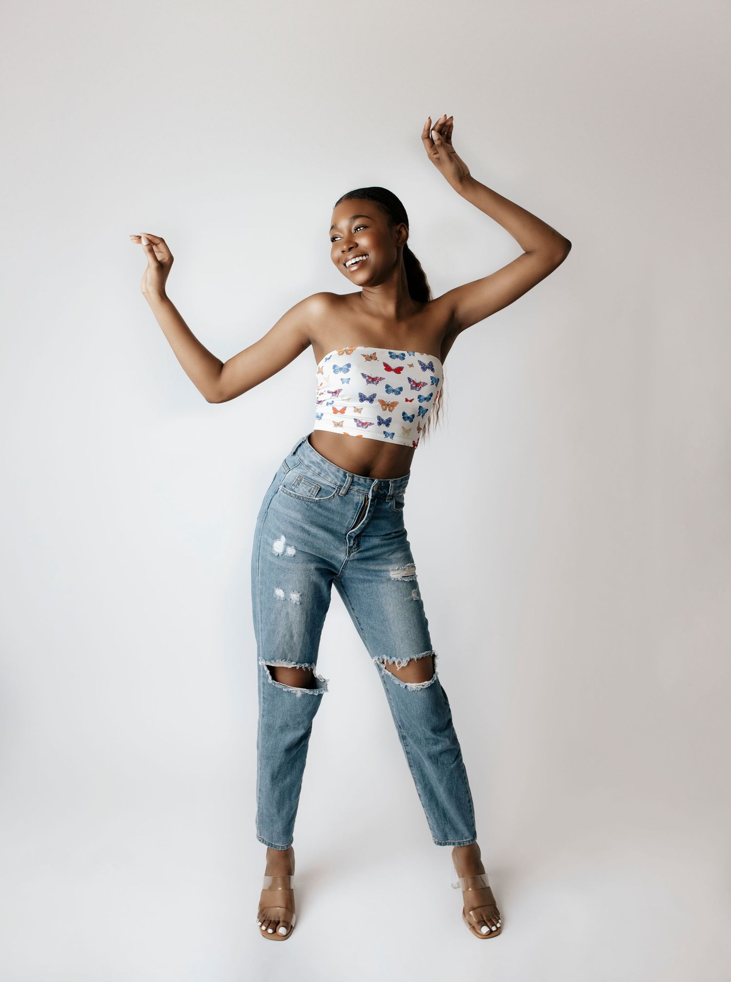 Joyful fashion shot of a strapless butterfly crop top paired with distressed denim jeans and neutral heels.