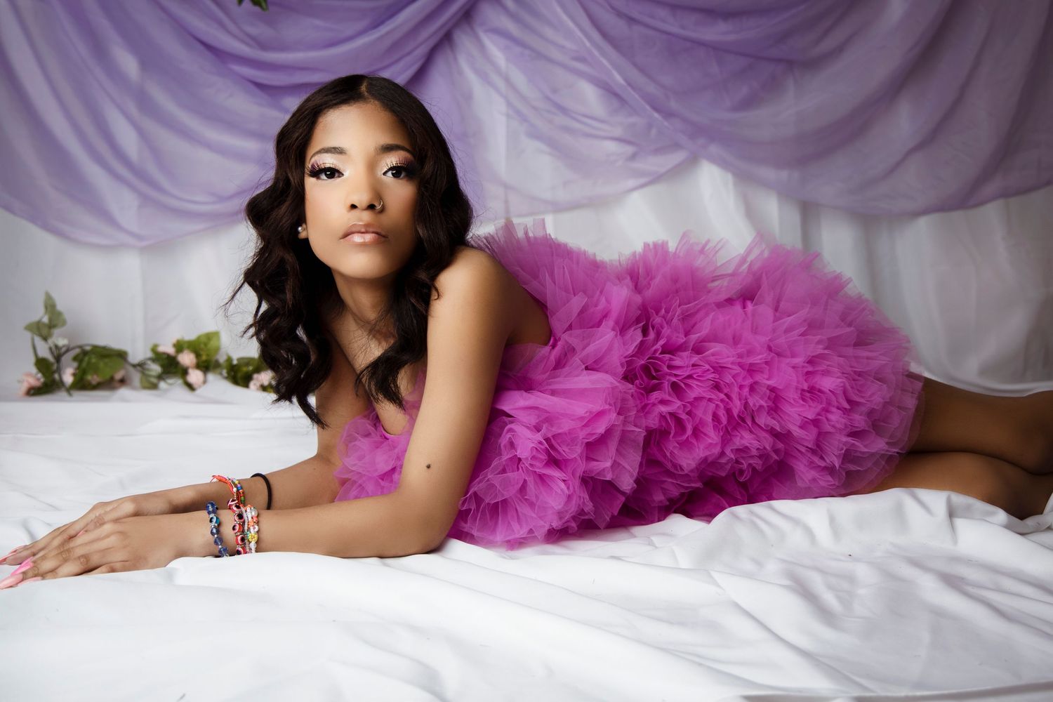Glamour portrait with purple tulle dress on white bedding.