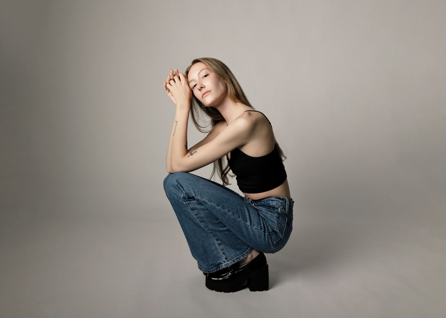 Casual portrait in denim and black top against neutral studio backdrop.