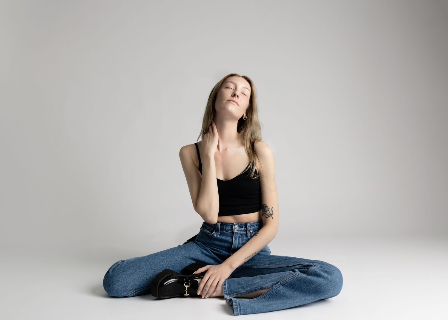 Portrait of woman in casual outfit sitting cross-legged on studio floor.