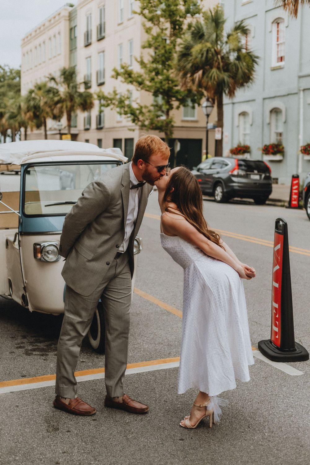 A couple shares a kiss in front of a vintage car