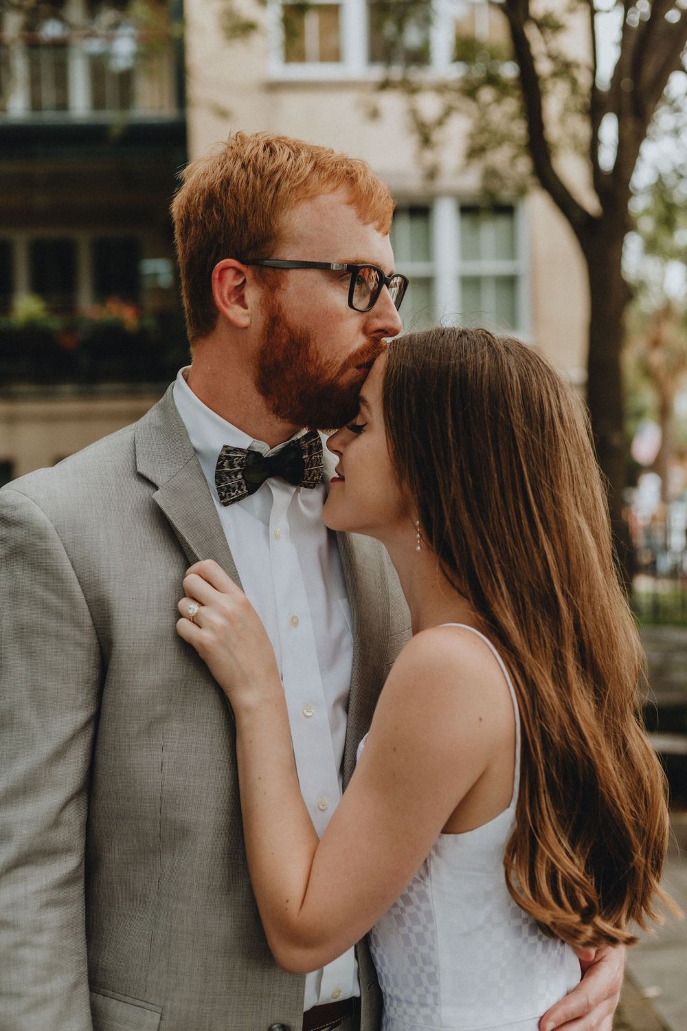 A man kisses a woman on the forehead while she holds his lapel