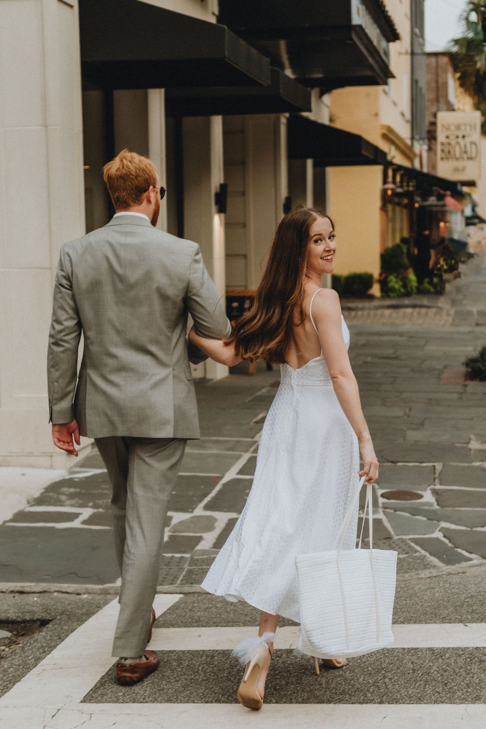 A man and woman stroll down the streets of Charleston while the woman looks back over her shoulder