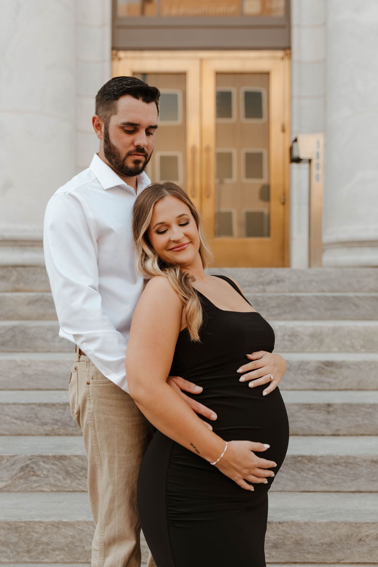 Expecting couple embrace on stone steps during sunset maternity photoshoot.