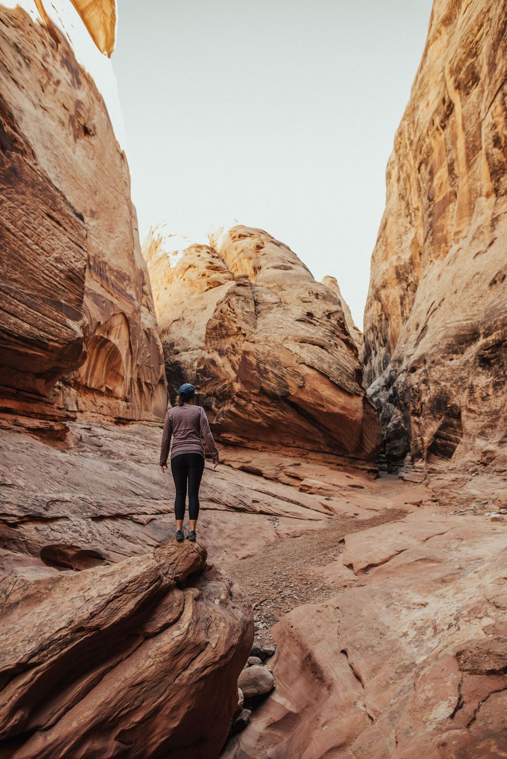 A hiker explores a narrow sandstone canyon with towering red rock walls in the desert wilderness.