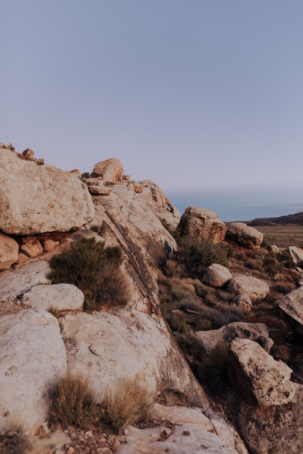 Desert rock formations and boulders stretch across a rugged landscape at sunset.
