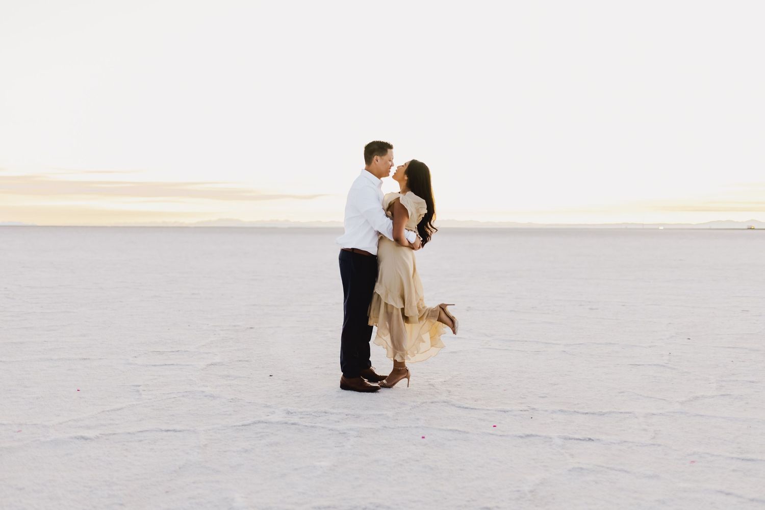 Couple embracing on white sand during a romantic beach photoshoot.