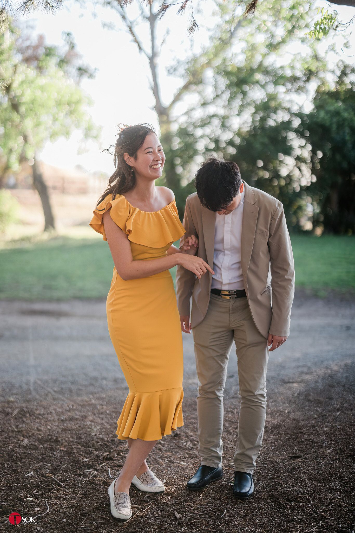 Couple in yellow dress and tan suit sharing playful moment outdoors.